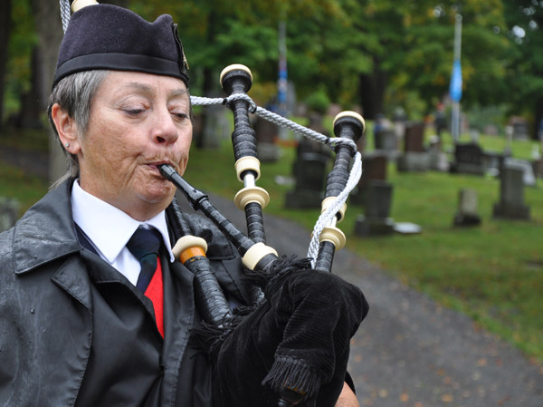 Pipe Major Susan March plays the bagpipes as the new United Nations flag is raised in the background at the Glenwood Cemetery Saturday morning. Photo Ross Lees