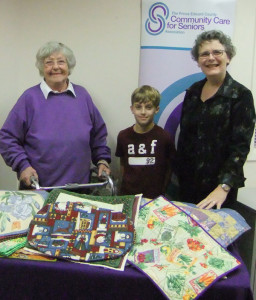 Joyce Young of the PEC Quilters’ Guild and her grandson Nick present quilted placemats to Debbie MacDonald Moynes, executive director of Community Care for Seniors.  